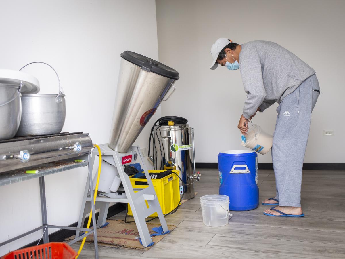 This picture shows Carlos Torres standing by the pasteurizer machine in a room, while loading a cooler with chicha.