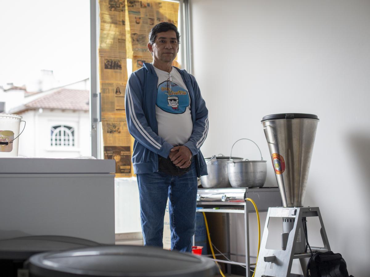 This picture shows Carlos Torres standing next to the pasteurizer machine with his arms crossed. The room appears to be his kitchen. 