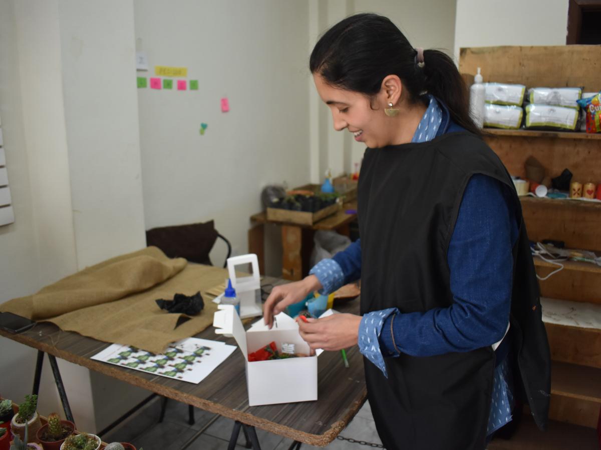 This picture shows Omaira in her store, preparing an decorative box to place a plant inside. 