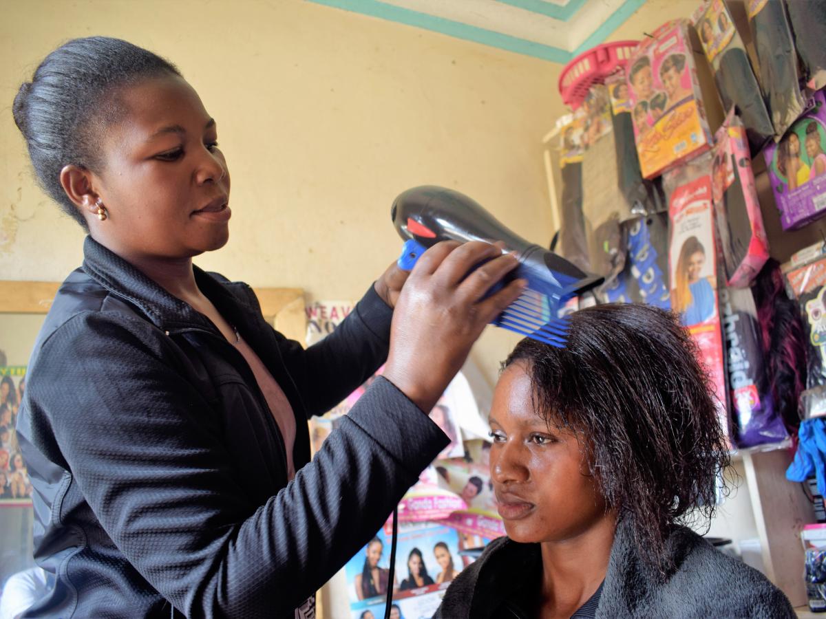 A female African hairdresser blow-drying a client's hair.