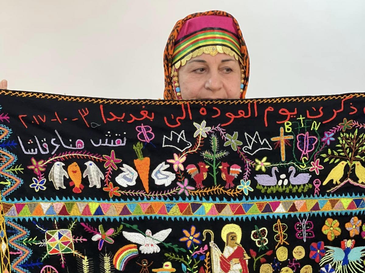A woman displays her brightly decorated tapestry.