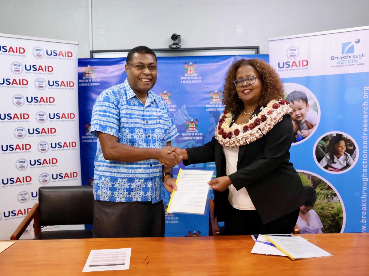 Left to right: Fiji Ministry of Health and Medical Services Acting Permanent Secretary Dr. Jemesa Tudravu and USAID Pacific Islands Mission Director Zema Semunegus do a handshake after signing a MOU to strengthen health communications in Fiji with support from USAID. The event included handover of media supplies for the Ministry’s communications team. Photo also shows USAID, USAID partner, Breakthrough ACTION, and Fiji Ministry of Health and Medical Services logo in the background.