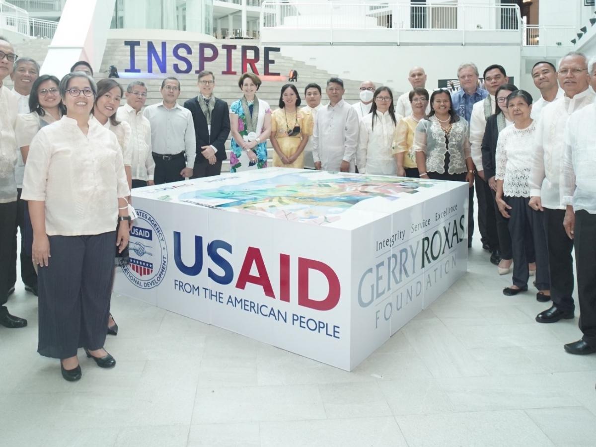 U.S. Ambassador to the Philippines MaryKay Carlson standing and gathered around the INSPIRE project box with representatives of the 11 organizations who received new grants under the USAID project.