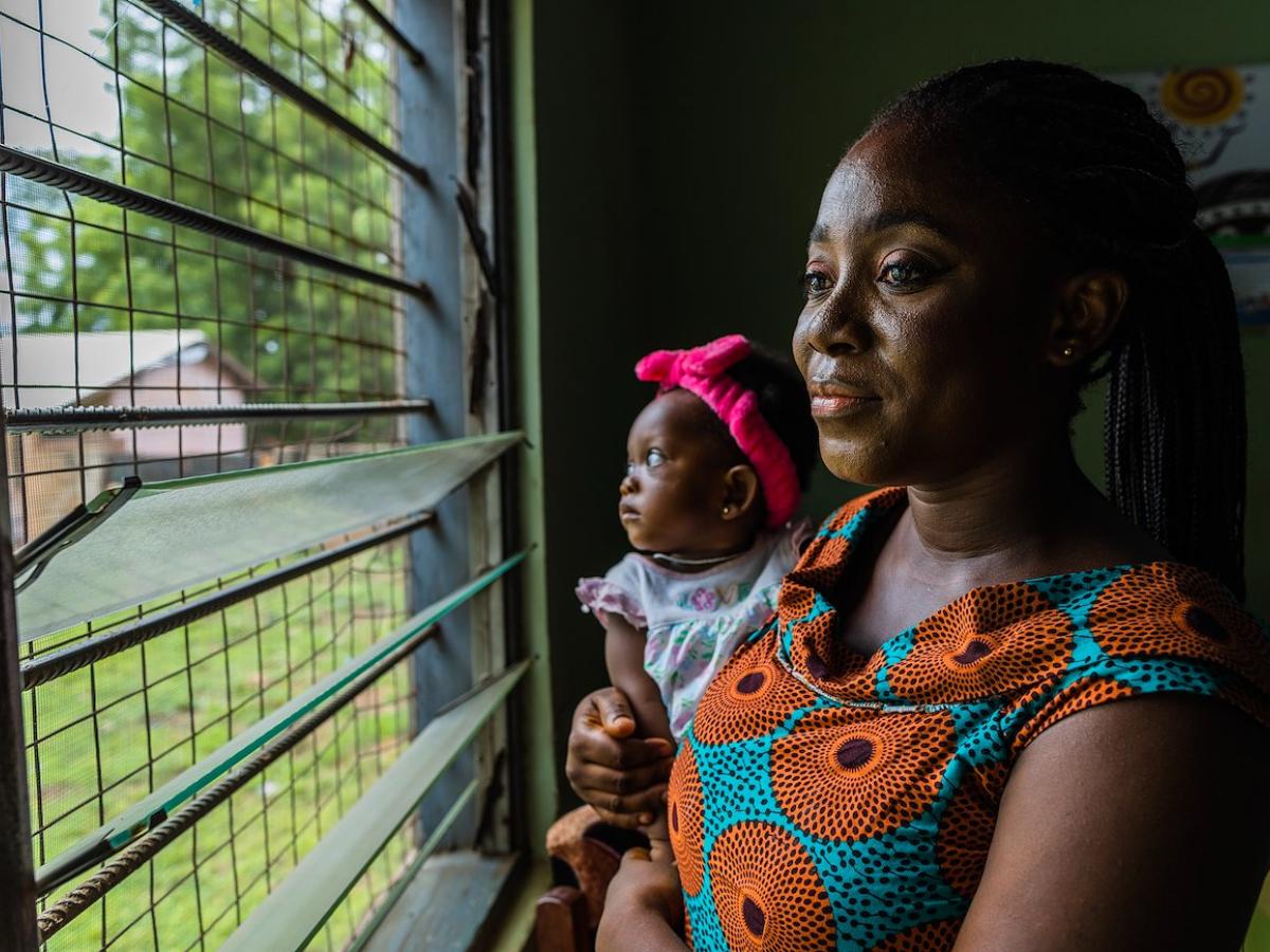 Patience, a client who was initially hesitant to get vaccinated but credits Adama for her decision to eventually get the COVID-19 vaccine, stands holding her infant daughter while looking out the clinic window. 