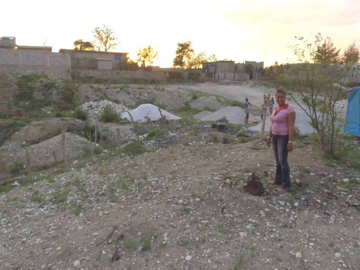 A woman stands at a plot of land in a Haitian village.