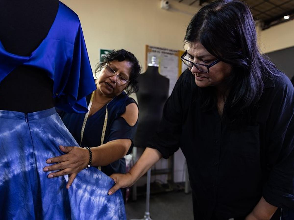 Two female Peruvian fashion designers inspect clothing on a mannequin.