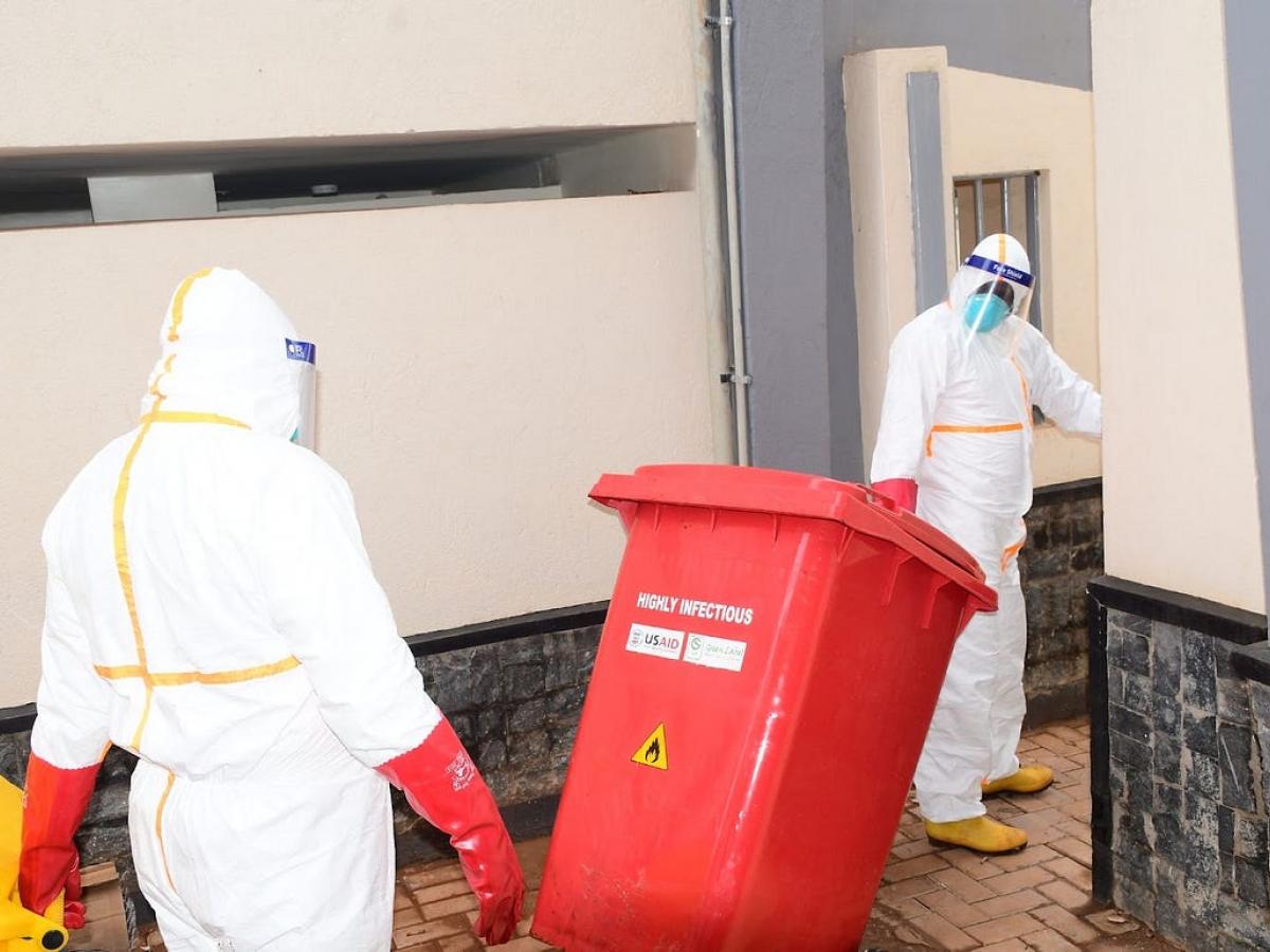 Two workers wearing protective clothing dispose of highly infectious waste from an Ebola isolation unit.