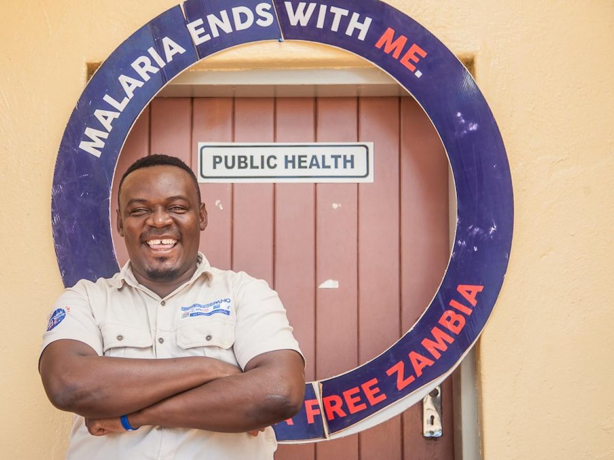 Man standing next to a door with a sign that states Malaria Ends with Me