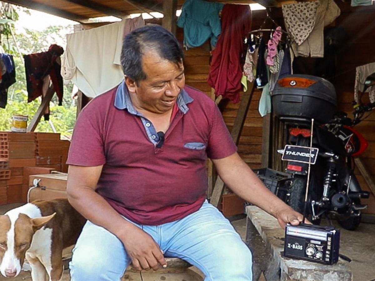 Un hombre sentado sonriendo junto a una radio portátil