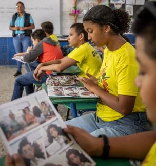 Students in bright yellow shirts read comic books at their desks at school