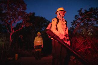 A member of the Second Indigenous Women's Fire Brigade is illuminated in the red glow of a wildfire.