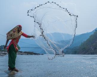 A woman throws a fishing net out over a river.