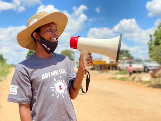 A USAID-supported community outreach worker speaks into a megaphone.