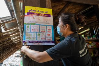 A woman wearing a face mask installs a COVID-19 social distancing poster in a village in Kayin State 