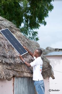 Un agent de Baobab Plus pose un panneau solaire sur une maison
