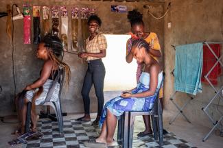 Two young Zambian women braid the hair of two women clients in a hair salon
