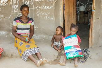 Joyce Tembo and her children pose with their insecticide-treated net (ITN) in front of their home.