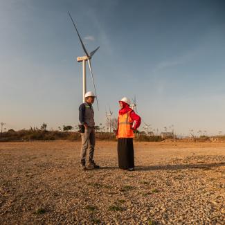 In front of a wind turbine in Tolo, South Sulawesi, two staff members of Indonesia's energy utility company exchange ideas. Since 2015, USAID has supported the generation of 438 megawatts of renewable, providing clean energy access to more than 3.3 million people.