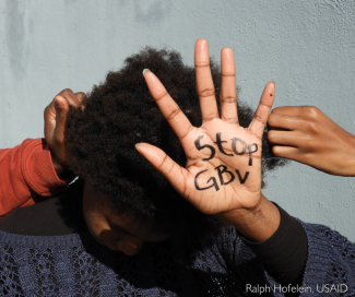 A woman shows her hand with the words "Stop GBV"