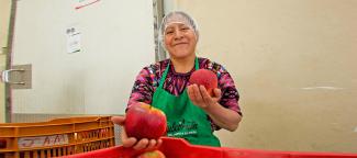 A smiling woman in an apron holds up the large fruit she is inspecting.