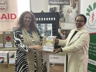 Two people holding a USAID-branded box and smiling in front of a camera