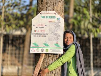 A female university student hugs a tree after participating in an iTree training hosted by the USAID COMPASS project.