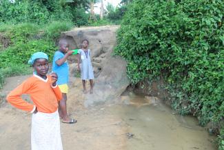 Three kids in front of the dirty river try to collect water