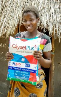 Joyce Tembo holds her insecticide-treated net in front of her home.