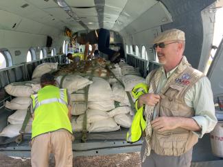 The inside of a helicopter, with large white sacks full of food and other relief items. Bags are packed into three rows, each row 4 bags high, strapped down for flight. 