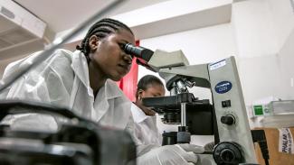 A lab technician in a health clinic exames a test sample through a microscope