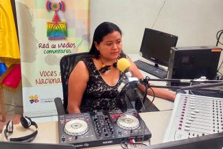 Una mujer indígena sentada y hablando frente al micrófono en la cabina de radio
