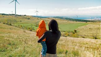Mother holding her son in rolling grassy hills. Wind turbines in the background.