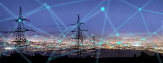 A cityscape at night with high power energy transmission towers in the foreground. A network of lines and dots of light are superimposed over the image to evoke the concept of the smart energy grid.