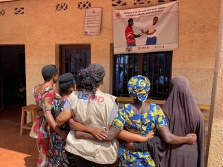 Four women stand with the USAID worker in front of the health center in Burundi supported through PEPFAR 