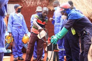 A head of household helps a spray operator mix the insecticide Isaya Mihayo