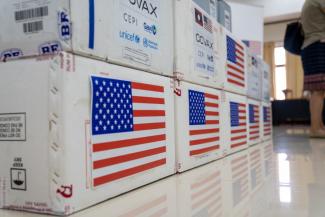 Stacked shipping boxes labeled with COVAX, CEPI, GAVI, UNICEF, World Health Organization and the U.S. flag