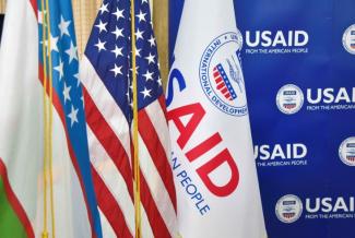 From left to right: Flag of Uzbekistan, Flag of the United States, and Flag with USAID logo in front of USIAD Step and Repeat
