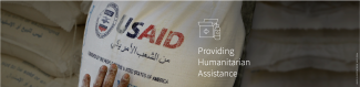 A hand touching a USAID branded bag representing Providing Humanitarian Assistance