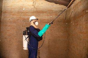 Man wearing protective clothing spray walls of a building