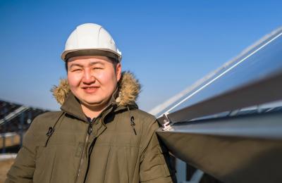 Close-up photo of a smiling man in a hard hat standing among photovoltaic arrays on a solar farm