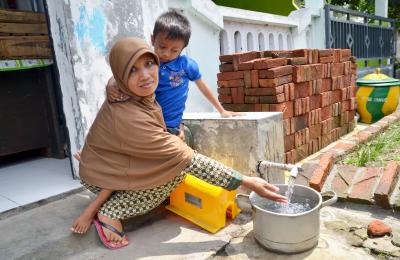 A water secure world means safe and sustainable access for all. Ibu Eko and her enjoying piped water services from the Sidoarjo District water utility (PDAM). The installation of the piped water connection was made possible through a microcredit scheme supported by USAID IUWASH. Without microcredit, it was unaffordable.