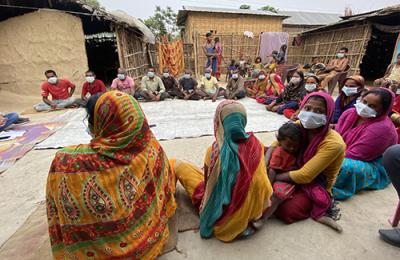 Members of a Dalit community in eastern Nepal sit on the ground in a semi circle during a listening session with USAID. The closest participants have their back to the camera; one woman faces the camera holding her baby.