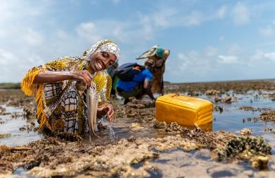 A smiling woman pulls an octopus she fishes out of the water of the Pate Marine Community Conservancy in Lamu County, Kenya
