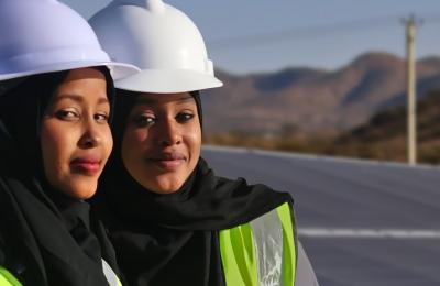 Close-up image of two female Somali engineering students wearing safety gear and head scarves in front of a field of solar photovoltaic panels.