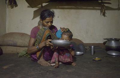 A woman feeds her daughter pakhal (boiled rice soaked overnight in water,) along with mushroom curry in their home in the Rayagada district of Odisha, India. Photo Credit: Rohit Jain