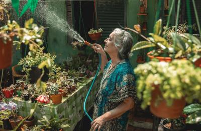 Olga uses a hose to water plants surrounding her in her nursery.
