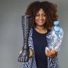 Martela Vania Uetela stands holding a prosthetic in one hand and plastic water bottles in another.