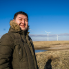 A man poses in a field in front of windmills.