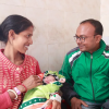 A couple, a man and a woman smile at each other while the woman holds their their baby. The group is sitting inside inside Ranchi District Hospital. Woman is holding their baby.