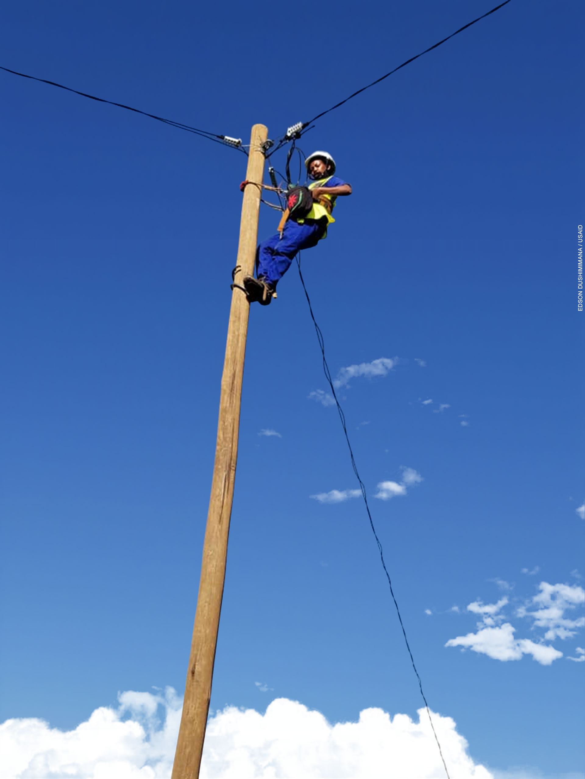 A female engineering apprentice atop a new electricity distribution pole works to complete its installation.